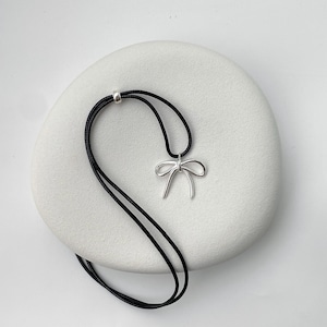 May include: A silver bow pendant necklace on a black cord.