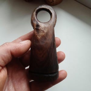 Hand holding a small, dark wooden figurine with a circular top and a carved triangular symbol on its body, likely a Slavic Panka doll or amulet.