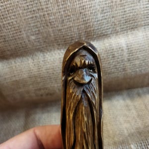 A 3.6-inch tall hand-carved linden wood figurine of a forest spirit. The figure has a long, flowing beard with deep textures and a face partially hidden under a hood. The dark brown stain highlights the artisan's hand-cut marks. This unique piece of Ukrainian folk art has a matte beeswax finish and a rustic, mystical appearance, shown against a neutral background.