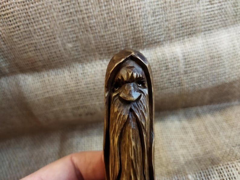 A 3.6-inch tall hand-carved linden wood figurine of a forest spirit. The figure has a long, flowing beard with deep textures and a face partially hidden under a hood. The dark brown stain highlights the artisan's hand-cut marks. This unique piece of Ukrainian folk art has a matte beeswax finish and a rustic, mystical appearance, shown against a neutral background.