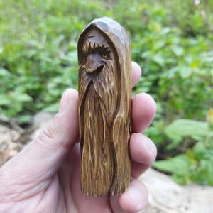 A 3.6-inch tall hand-carved linden wood figurine of a forest spirit. The figure has a long, flowing beard with deep textures and a face partially hidden under a hood. The dark brown stain highlights the artisan's hand-cut marks. This unique piece of Ukrainian folk art has a matte beeswax finish and a rustic, mystical appearance, shown against a neutral background.
