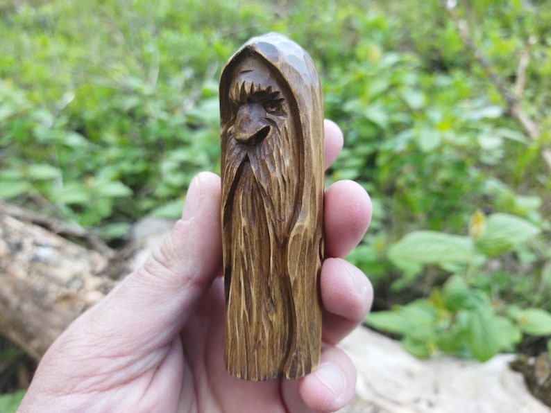 A 3.6-inch tall hand-carved linden wood figurine of a forest spirit. The figure has a long, flowing beard with deep textures and a face partially hidden under a hood. The dark brown stain highlights the artisan's hand-cut marks. This unique piece of Ukrainian folk art has a matte beeswax finish and a rustic, mystical appearance, shown against a neutral background.