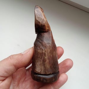 Hand holding a small, dark wooden figurine with a circular top and a carved triangular symbol on its body, likely a Slavic Panka doll or amulet.