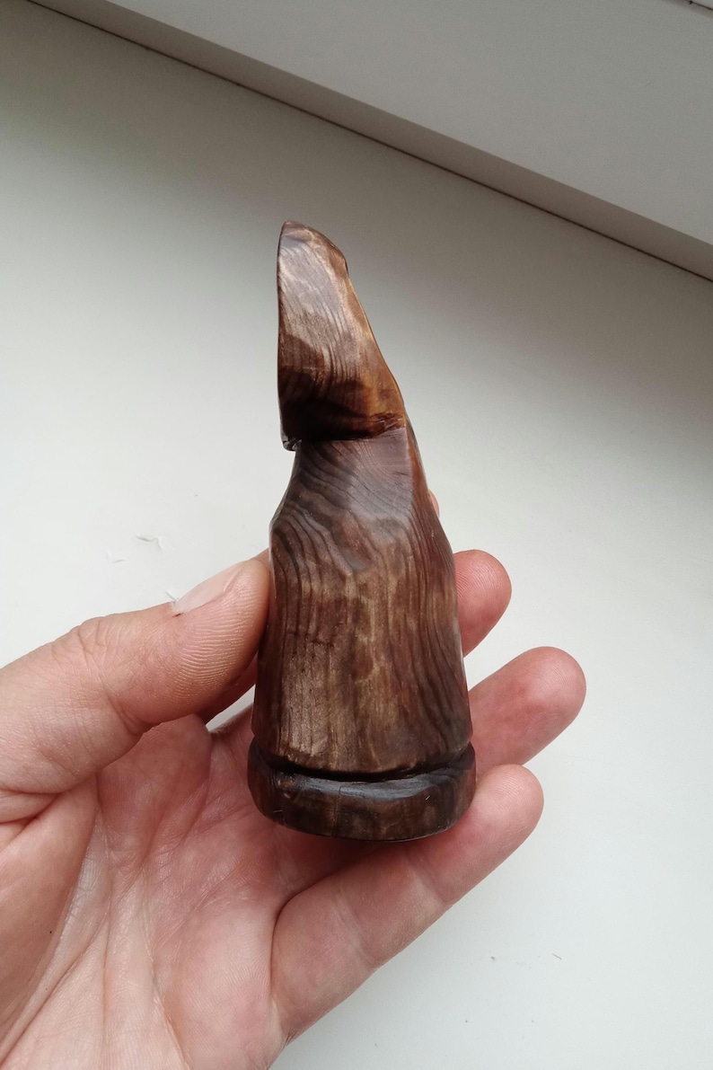 Hand holding a small, dark wooden figurine with a circular top and a carved triangular symbol on its body, likely a Slavic Panka doll or amulet.