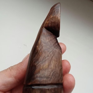 Hand holding a small, dark wooden figurine with a circular top and a carved triangular symbol on its body, likely a Slavic Panka doll or amulet.