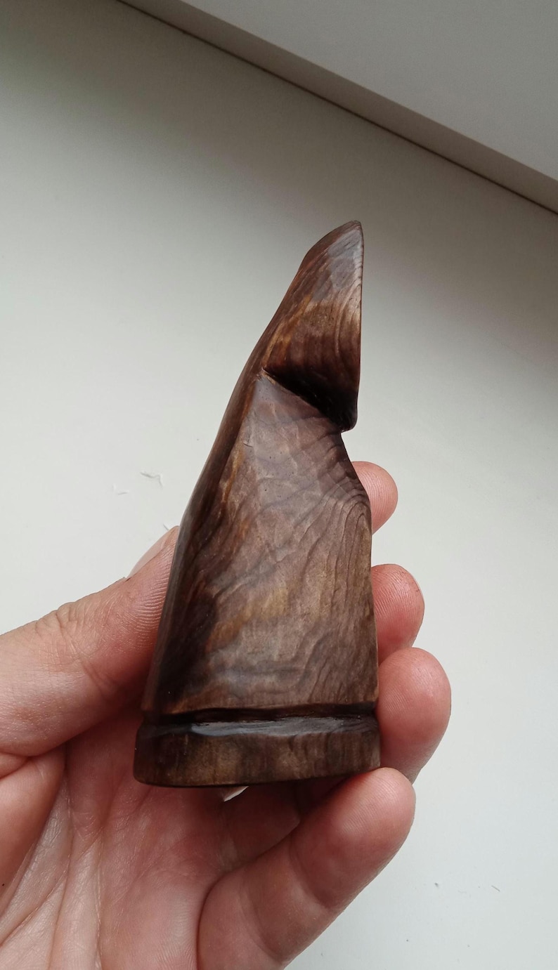 Hand holding a small, dark wooden figurine with a circular top and a carved triangular symbol on its body, likely a Slavic Panka doll or amulet.