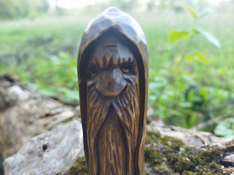 A 3.6-inch tall hand-carved linden wood figurine of a forest spirit. The figure has a long, flowing beard with deep textures and a face partially hidden under a hood. The dark brown stain highlights the artisan's hand-cut marks. This unique piece of Ukrainian folk art has a matte beeswax finish and a rustic, mystical appearance, shown against a neutral background.