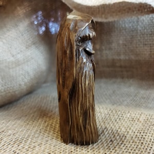 A 3.6-inch tall hand-carved linden wood figurine of a forest spirit. The figure has a long, flowing beard with deep textures and a face partially hidden under a hood. The dark brown stain highlights the artisan's hand-cut marks. This unique piece of Ukrainian folk art has a matte beeswax finish and a rustic, mystical appearance, shown against a neutral background.