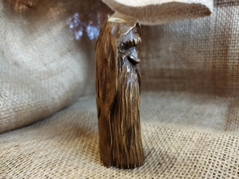 A 3.6-inch tall hand-carved linden wood figurine of a forest spirit. The figure has a long, flowing beard with deep textures and a face partially hidden under a hood. The dark brown stain highlights the artisan's hand-cut marks. This unique piece of Ukrainian folk art has a matte beeswax finish and a rustic, mystical appearance, shown against a neutral background.