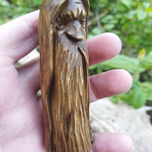 A 3.6-inch tall hand-carved linden wood figurine of a forest spirit. The figure has a long, flowing beard with deep textures and a face partially hidden under a hood. The dark brown stain highlights the artisan's hand-cut marks. This unique piece of Ukrainian folk art has a matte beeswax finish and a rustic, mystical appearance, shown against a neutral background.