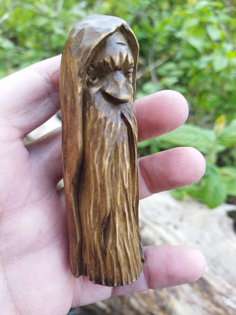 A 3.6-inch tall hand-carved linden wood figurine of a forest spirit. The figure has a long, flowing beard with deep textures and a face partially hidden under a hood. The dark brown stain highlights the artisan's hand-cut marks. This unique piece of Ukrainian folk art has a matte beeswax finish and a rustic, mystical appearance, shown against a neutral background.