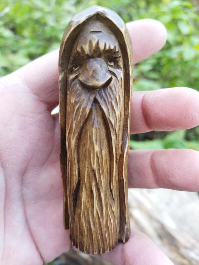 A 3.6-inch tall hand-carved linden wood figurine of a forest spirit. The figure has a long, flowing beard with deep textures and a face partially hidden under a hood. The dark brown stain highlights the artisan's hand-cut marks. This unique piece of Ukrainian folk art has a matte beeswax finish and a rustic, mystical appearance, shown against a neutral background.