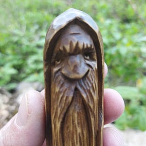 A 3.6-inch tall hand-carved linden wood figurine of a forest spirit. The figure has a long, flowing beard with deep textures and a face partially hidden under a hood. The dark brown stain highlights the artisan's hand-cut marks. This unique piece of Ukrainian folk art has a matte beeswax finish and a rustic, mystical appearance, shown against a neutral background.