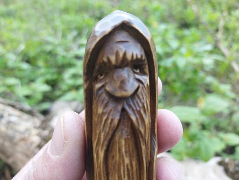 A 3.6-inch tall hand-carved linden wood figurine of a forest spirit. The figure has a long, flowing beard with deep textures and a face partially hidden under a hood. The dark brown stain highlights the artisan's hand-cut marks. This unique piece of Ukrainian folk art has a matte beeswax finish and a rustic, mystical appearance, shown against a neutral background.