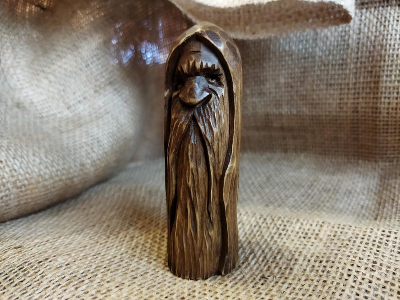 A 3.6-inch tall hand-carved linden wood figurine of a forest spirit. The figure has a long, flowing beard with deep textures and a face partially hidden under a hood. The dark brown stain highlights the artisan's hand-cut marks. This unique piece of Ukrainian folk art has a matte beeswax finish and a rustic, mystical appearance, shown against a neutral background.