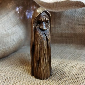 A 3.6-inch tall hand-carved linden wood figurine of a forest spirit. The figure has a long, flowing beard with deep textures and a face partially hidden under a hood. The dark brown stain highlights the artisan's hand-cut marks. This unique piece of Ukrainian folk art has a matte beeswax finish and a rustic, mystical appearance, shown against a neutral background.