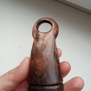 Hand holding a small, dark wooden figurine with a circular top and a carved triangular symbol on its body, likely a Slavic Panka doll or amulet.