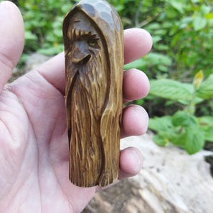 A 3.6-inch tall hand-carved linden wood figurine of a forest spirit. The figure has a long, flowing beard with deep textures and a face partially hidden under a hood. The dark brown stain highlights the artisan's hand-cut marks. This unique piece of Ukrainian folk art has a matte beeswax finish and a rustic, mystical appearance, shown against a neutral background.