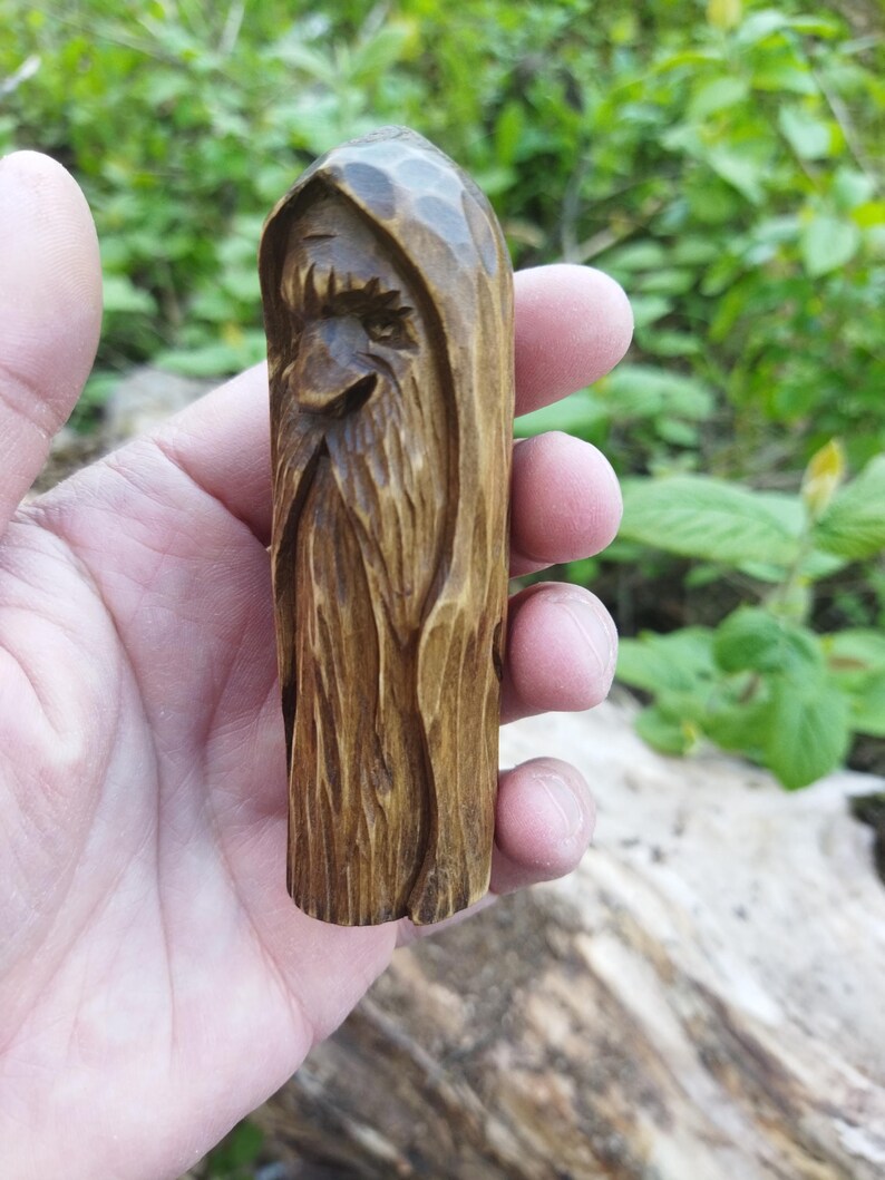 A 3.6-inch tall hand-carved linden wood figurine of a forest spirit. The figure has a long, flowing beard with deep textures and a face partially hidden under a hood. The dark brown stain highlights the artisan's hand-cut marks. This unique piece of Ukrainian folk art has a matte beeswax finish and a rustic, mystical appearance, shown against a neutral background.