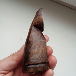 Hand holding a small, dark wooden figurine with a circular top and a carved triangular symbol on its body, likely a Slavic Panka doll or amulet.