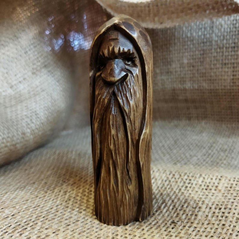 A 3.6-inch tall hand-carved linden wood figurine of a forest spirit. The figure has a long, flowing beard with deep textures and a face partially hidden under a hood. The dark brown stain highlights the artisan's hand-cut marks. This unique piece of Ukrainian folk art has a matte beeswax finish and a rustic, mystical appearance, shown against a neutral background.