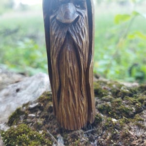 A 3.6-inch tall hand-carved linden wood figurine of a forest spirit. The figure has a long, flowing beard with deep textures and a face partially hidden under a hood. The dark brown stain highlights the artisan's hand-cut marks. This unique piece of Ukrainian folk art has a matte beeswax finish and a rustic, mystical appearance, shown against a neutral background.