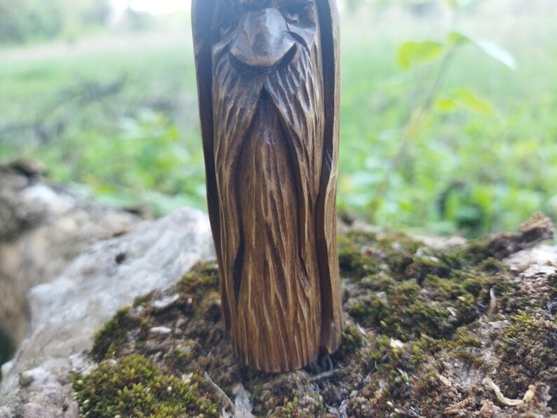 A 3.6-inch tall hand-carved linden wood figurine of a forest spirit. The figure has a long, flowing beard with deep textures and a face partially hidden under a hood. The dark brown stain highlights the artisan's hand-cut marks. This unique piece of Ukrainian folk art has a matte beeswax finish and a rustic, mystical appearance, shown against a neutral background.