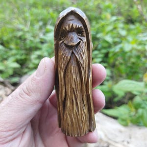 A 3.6-inch tall hand-carved linden wood figurine of a forest spirit. The figure has a long, flowing beard with deep textures and a face partially hidden under a hood. The dark brown stain highlights the artisan's hand-cut marks. This unique piece of Ukrainian folk art has a matte beeswax finish and a rustic, mystical appearance, shown against a neutral background.