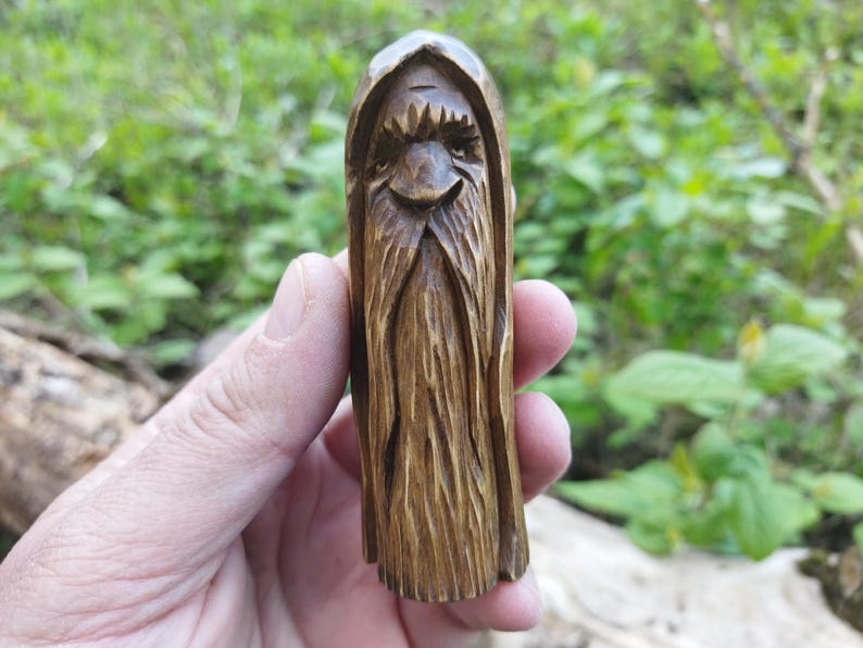 A 3.6-inch tall hand-carved linden wood figurine of a forest spirit. The figure has a long, flowing beard with deep textures and a face partially hidden under a hood. The dark brown stain highlights the artisan's hand-cut marks. This unique piece of Ukrainian folk art has a matte beeswax finish and a rustic, mystical appearance, shown against a neutral background.