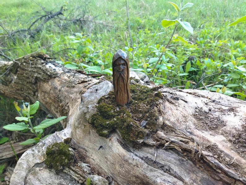 A 3.6-inch tall hand-carved linden wood figurine of a forest spirit. The figure has a long, flowing beard with deep textures and a face partially hidden under a hood. The dark brown stain highlights the artisan's hand-cut marks. This unique piece of Ukrainian folk art has a matte beeswax finish and a rustic, mystical appearance, shown against a neutral background.