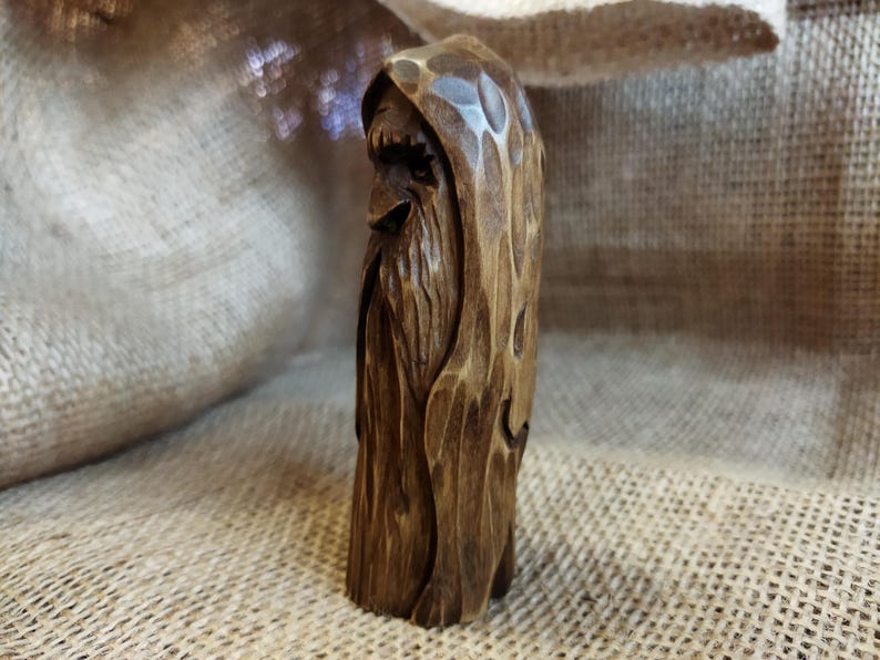 A 3.6-inch tall hand-carved linden wood figurine of a forest spirit. The figure has a long, flowing beard with deep textures and a face partially hidden under a hood. The dark brown stain highlights the artisan's hand-cut marks. This unique piece of Ukrainian folk art has a matte beeswax finish and a rustic, mystical appearance, shown against a neutral background.
