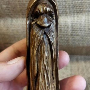 A 3.6-inch tall hand-carved linden wood figurine of a forest spirit. The figure has a long, flowing beard with deep textures and a face partially hidden under a hood. The dark brown stain highlights the artisan's hand-cut marks. This unique piece of Ukrainian folk art has a matte beeswax finish and a rustic, mystical appearance, shown against a neutral background.