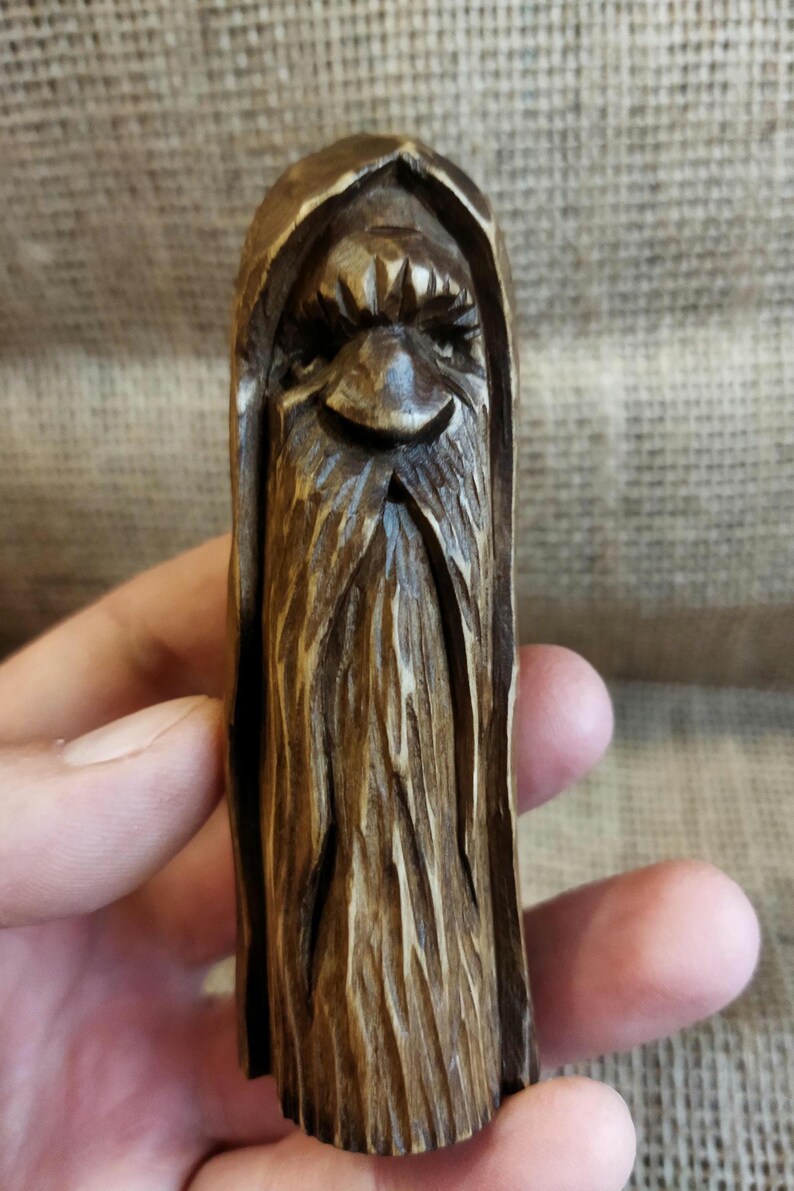 A 3.6-inch tall hand-carved linden wood figurine of a forest spirit. The figure has a long, flowing beard with deep textures and a face partially hidden under a hood. The dark brown stain highlights the artisan's hand-cut marks. This unique piece of Ukrainian folk art has a matte beeswax finish and a rustic, mystical appearance, shown against a neutral background.
