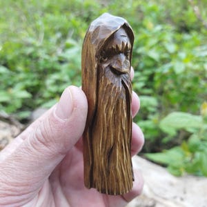 A 3.6-inch tall hand-carved linden wood figurine of a forest spirit. The figure has a long, flowing beard with deep textures and a face partially hidden under a hood. The dark brown stain highlights the artisan's hand-cut marks. This unique piece of Ukrainian folk art has a matte beeswax finish and a rustic, mystical appearance, shown against a neutral background.