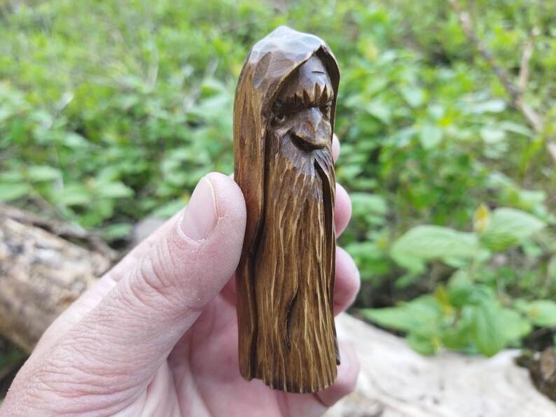 A 3.6-inch tall hand-carved linden wood figurine of a forest spirit. The figure has a long, flowing beard with deep textures and a face partially hidden under a hood. The dark brown stain highlights the artisan's hand-cut marks. This unique piece of Ukrainian folk art has a matte beeswax finish and a rustic, mystical appearance, shown against a neutral background.