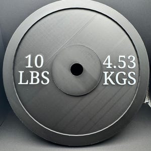 May include: A black weight plate with white text that reads "10 LBS" and "4.53 KGS".