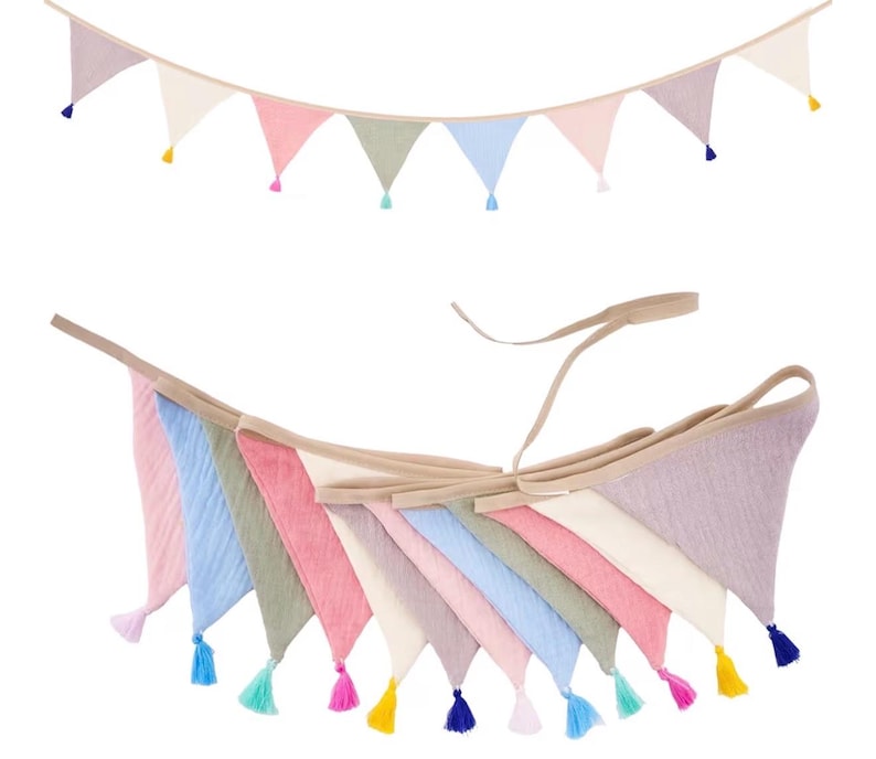 May include: A fabric bunting banner featuring a series of triangular flags in pastel shades of pink, blue, green, cream, and lavender. Each triangular flag is finished with a small, matching colored tassel attached to the bottom point.