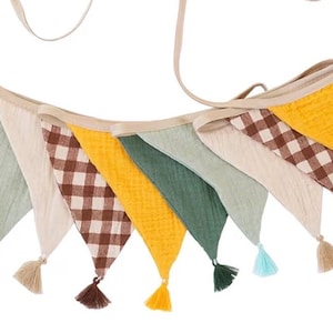 May include: A fabric bunting banner featuring triangular flags in solid mustard yellow, sage green, and cream, alternating with brown and white gingham checkered flags. Each flag is finished with a small matching tassel at the bottom point.
