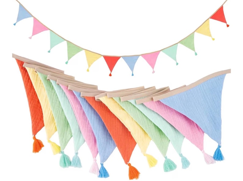 May include: A decorative bunting banner featuring triangular fabric flags in pastel shades of blue, pink, green, yellow, and orange. The flags are attached to a tan fabric cord, and each individual flag features a matching colored tassel.