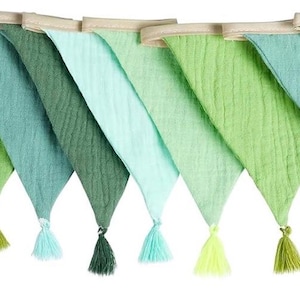 May include: A decorative bunting banner featuring ten triangular fabric flags in various shades of green, ranging from light mint to deep forest green. Each flag is made of textured muslin fabric and is finished with a matching tassel at the point.