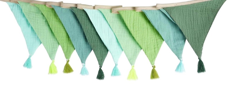May include: A decorative bunting banner featuring ten triangular fabric flags in various shades of green, ranging from light mint to deep forest green. Each flag is made of textured muslin fabric and is finished with a matching tassel at the point.