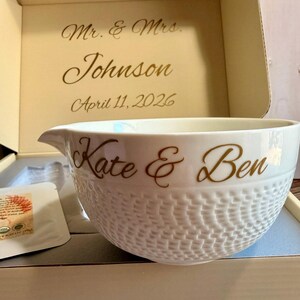 May include: A white ceramic mixing bowl with a basketweave pattern. The bowl is inscribed with "Kate & Ben" in gold script. The box behind the bowl is inscribed with "Mr. & Mrs. Johnson" and the date "April 11, 2026".