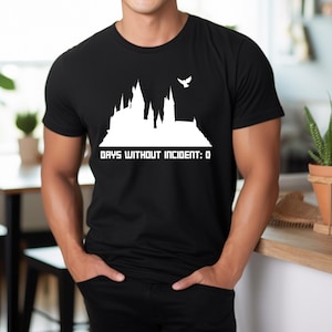 May include: A black t-shirt with a white silhouette of Hogwarts castle and a bird flying above it. The text "Days Without Incident: 0" is printed below the castle.