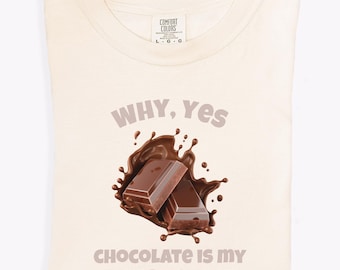 Könnte beinhalten: Cremefarbenes T-Shirt mit dem Text "WHY, Yes" und "CHOCOLATE IS MY FAVORITE FOOD" in brauner Schrift. Die Grafik zeigt zwei Schokoladenriegel mit einem Schokoladenspritzer-Design.