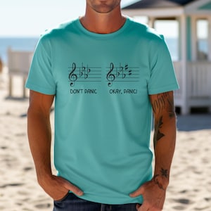 May include: A turquoise t-shirt with a musical notation design. The design features two treble clefs with notes and the text "Don't Panic" and "Okay, Panic!"