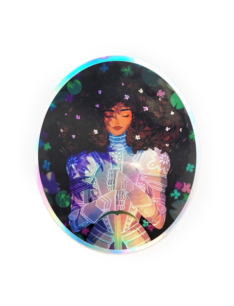 May include: A round sticker with a holographic finish featuring a woman with dark curly hair wearing armor and a crown of flowers. The background is a dark green with flowers and leaves.