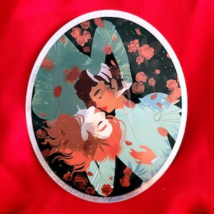 May include: A round sticker with a romantic illustration of two people embracing. The sticker features a dark background with a scattering of red flowers and a silver border.