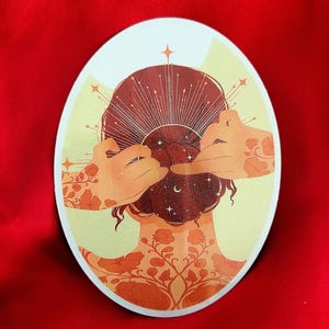 May include: A sticker featuring a woman with a bun in her hair, decorated with stars and a crescent moon. Her hands are holding the bun, and her back is adorned with floral tattoos.