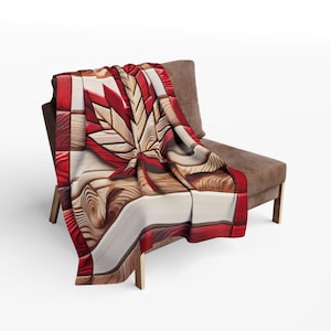 May include: A decorative throw blanket draped over a brown chair. The blanket features a large, stylized maple leaf design in shades of red, cream, and brown, with a wood grain pattern. The blanket's border is a solid red.