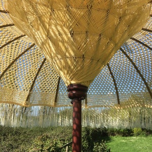 May include: A large, woven, beige patio umbrella with a fringe border. The umbrella is made of natural materials and has a wooden pole.